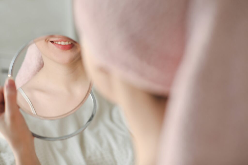 A woman smiling into a mirror while at the Dentist recieving great care thanks to AI and Augmented Reality technology now being used.