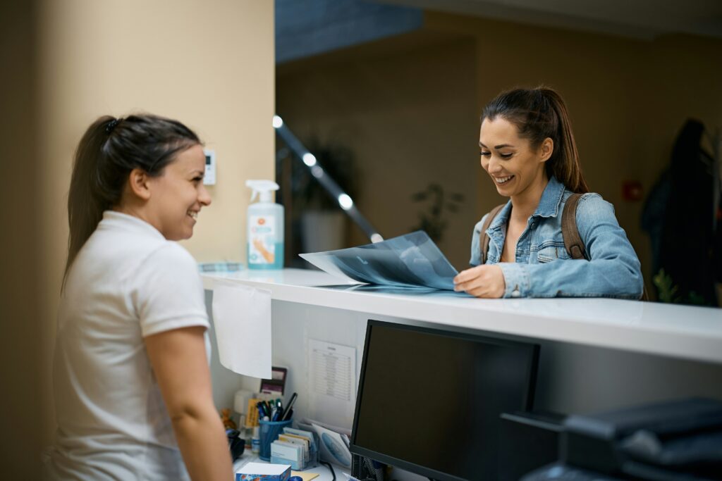 A woman checking in with a female receptionist in a medical office that has updated AI systems to better serve their patients